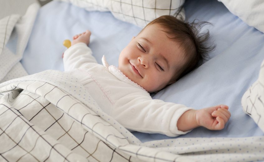 Smiling baby girl lying on a bed sleeping on blue sheets